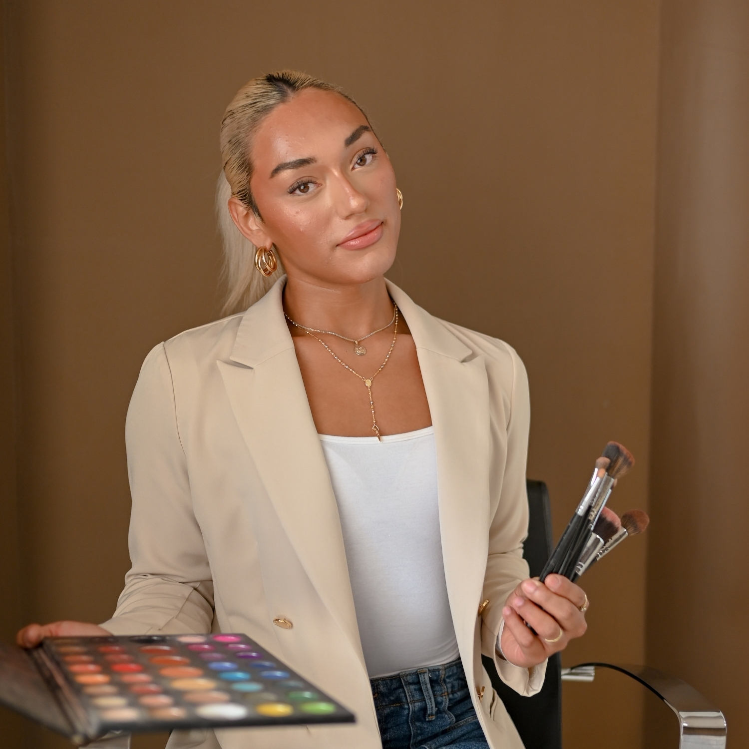 Beauty student holding makeup brushes and palette during professional branding photoshoot.