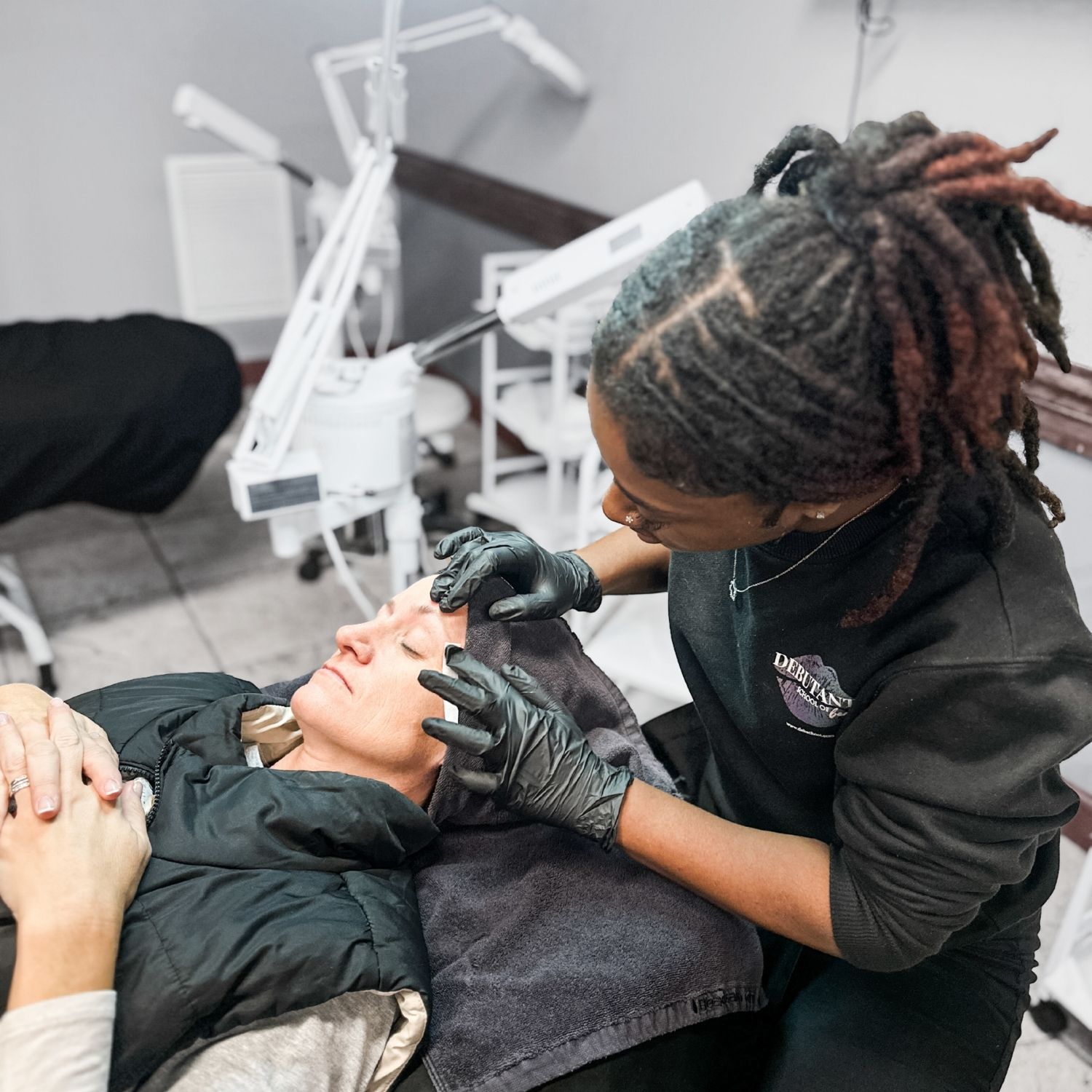 A black student is performing an eyebrow wax on a white middle aged female.